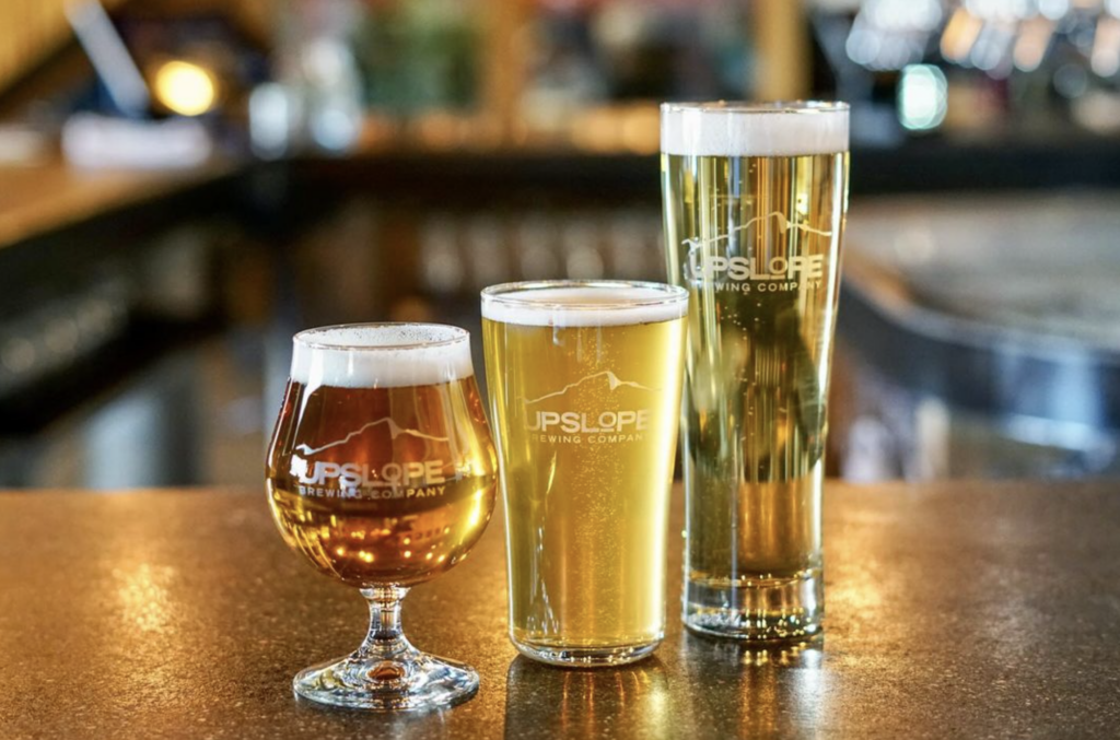 Three different shaped glasses on a restaurant bar each filled with a different beer